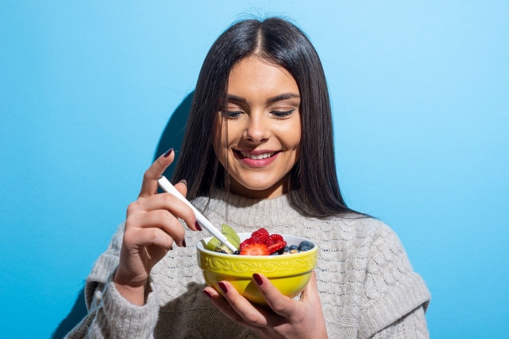 Young woman eating muesli breakfast on blue background.Studio Shot